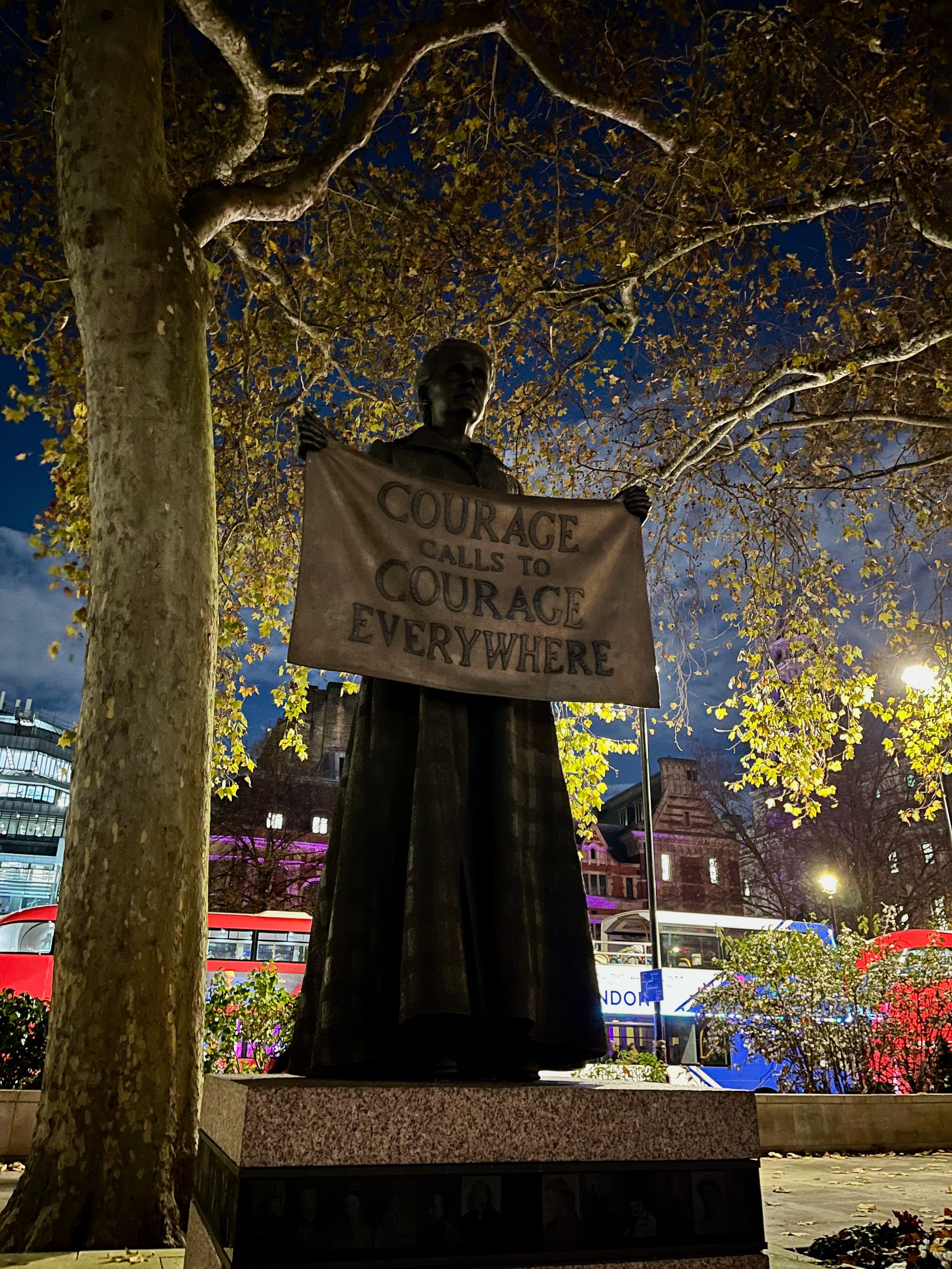 A statue of a woman holding a sign which reads "Courage calls to courage everywhere". it is night time