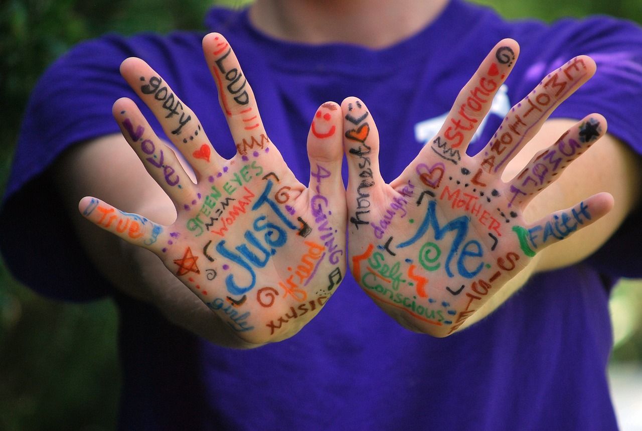 Two white hands are held out. words in different coloured ink are painted on the palms and fingers