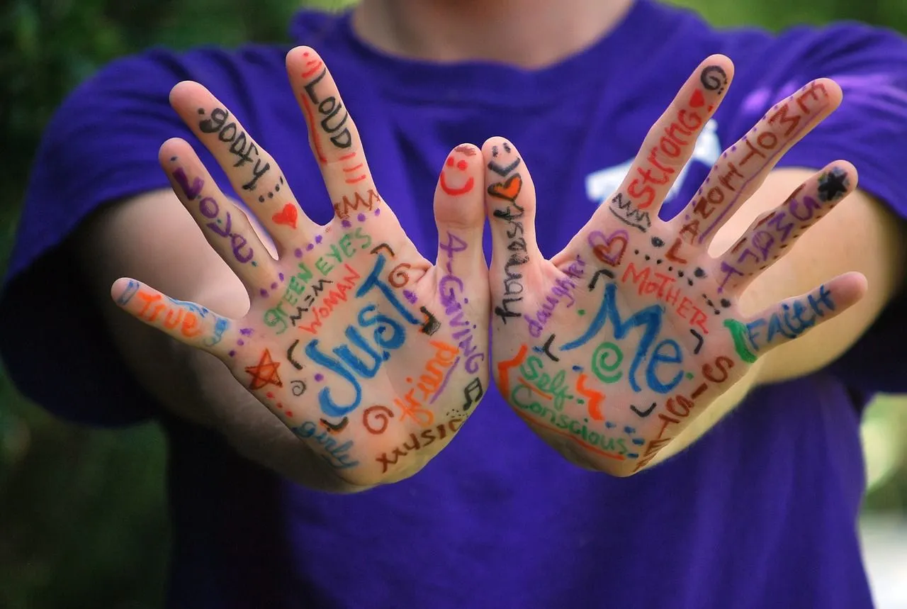 Two white hands are held out. words in different coloured ink are painted on the palms and fingers