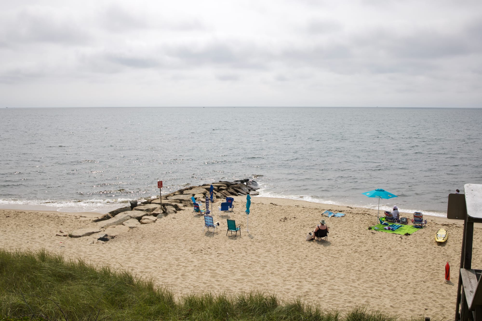 A photo of a beach on Cape Cod. A rock jetty is in the center of the frame, and there are some small silhouetted figures on the beach.