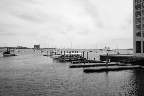 A monochrome image of a dock in Boston with small ships in the background 