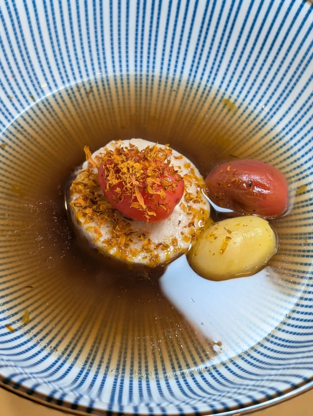A composed dish of egg, tomato and potato in a clear amber broth