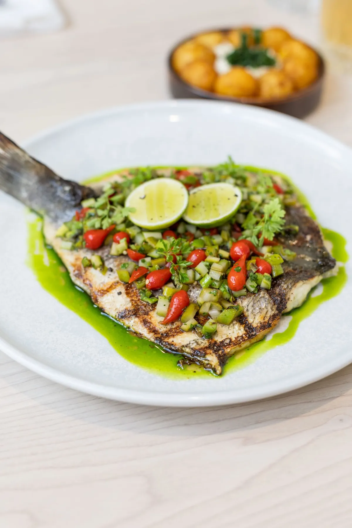 A grilled fish topped with chopped peppers, herbs and lime on a bright green herb sauce