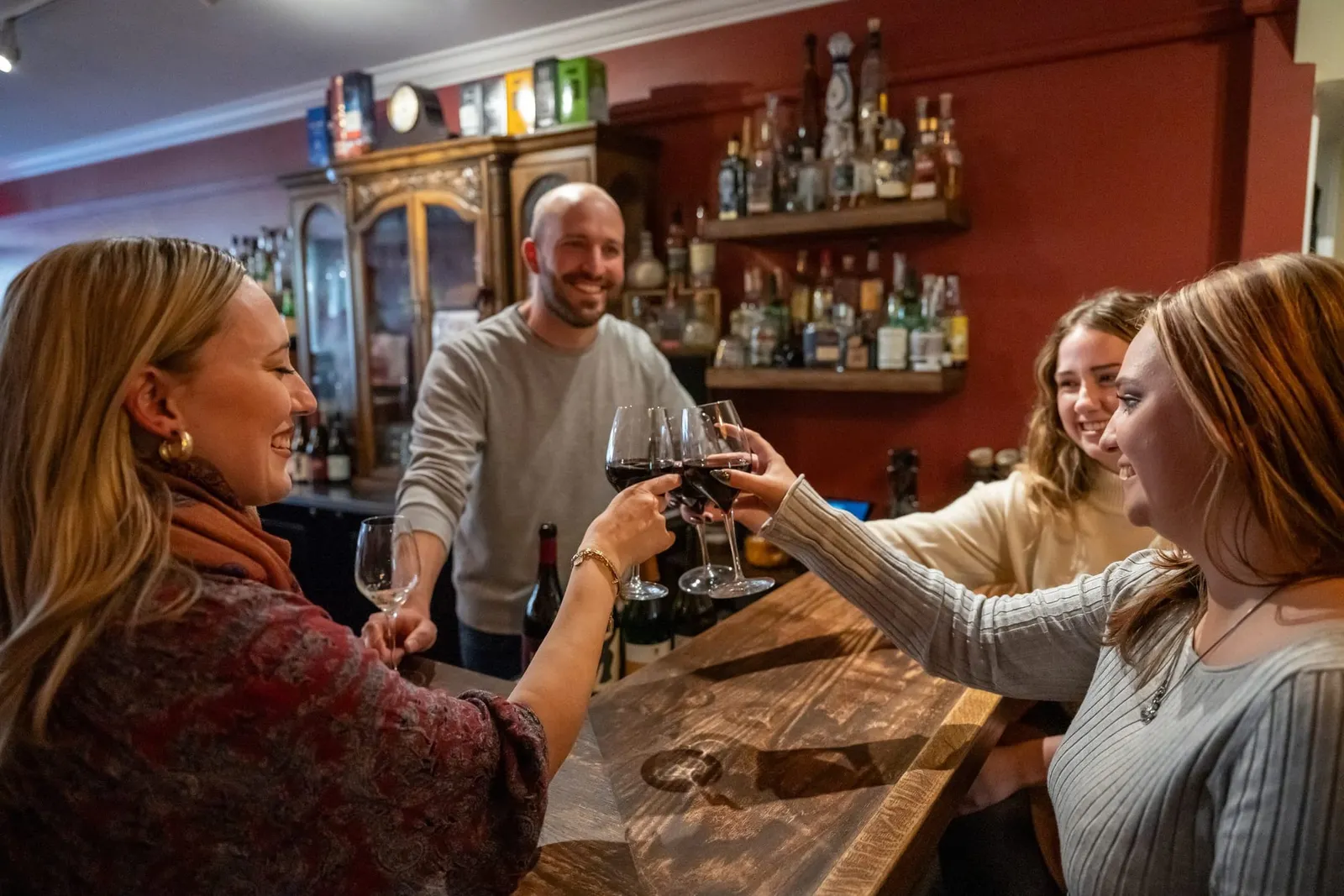 Friends raising glasses of red wine together at a warmly lit bar