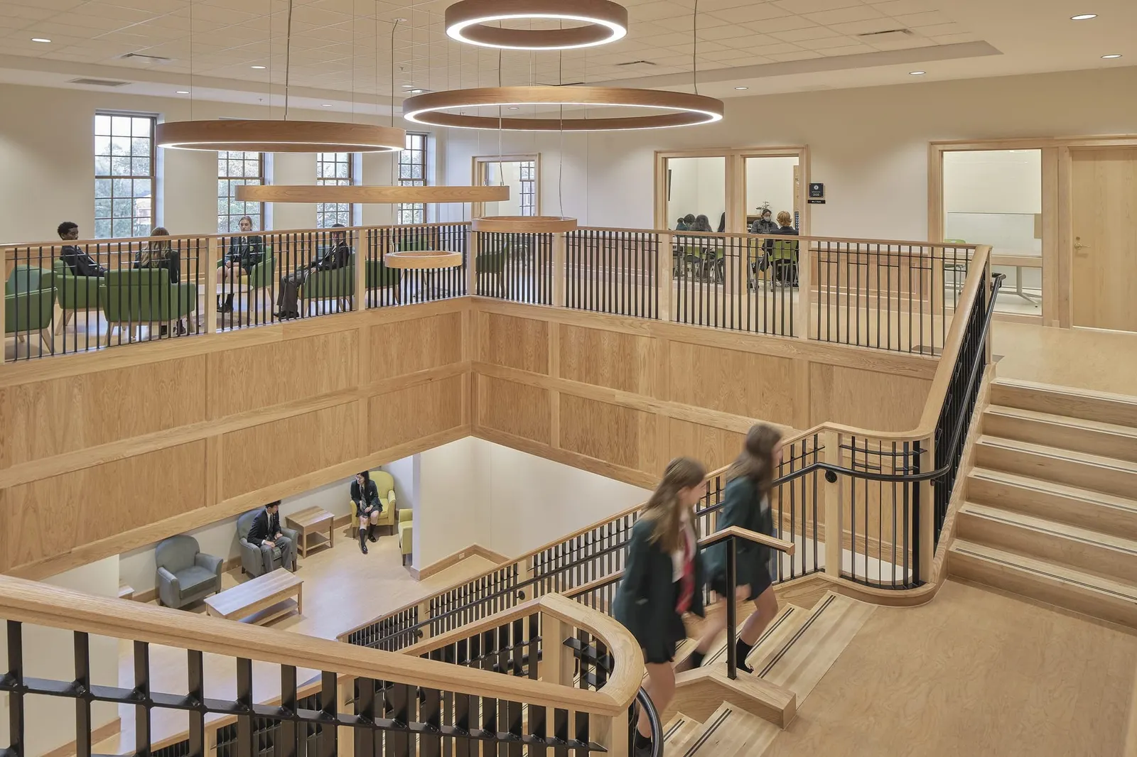 Students crossing the open wooden staircase of the school's bright learning commons