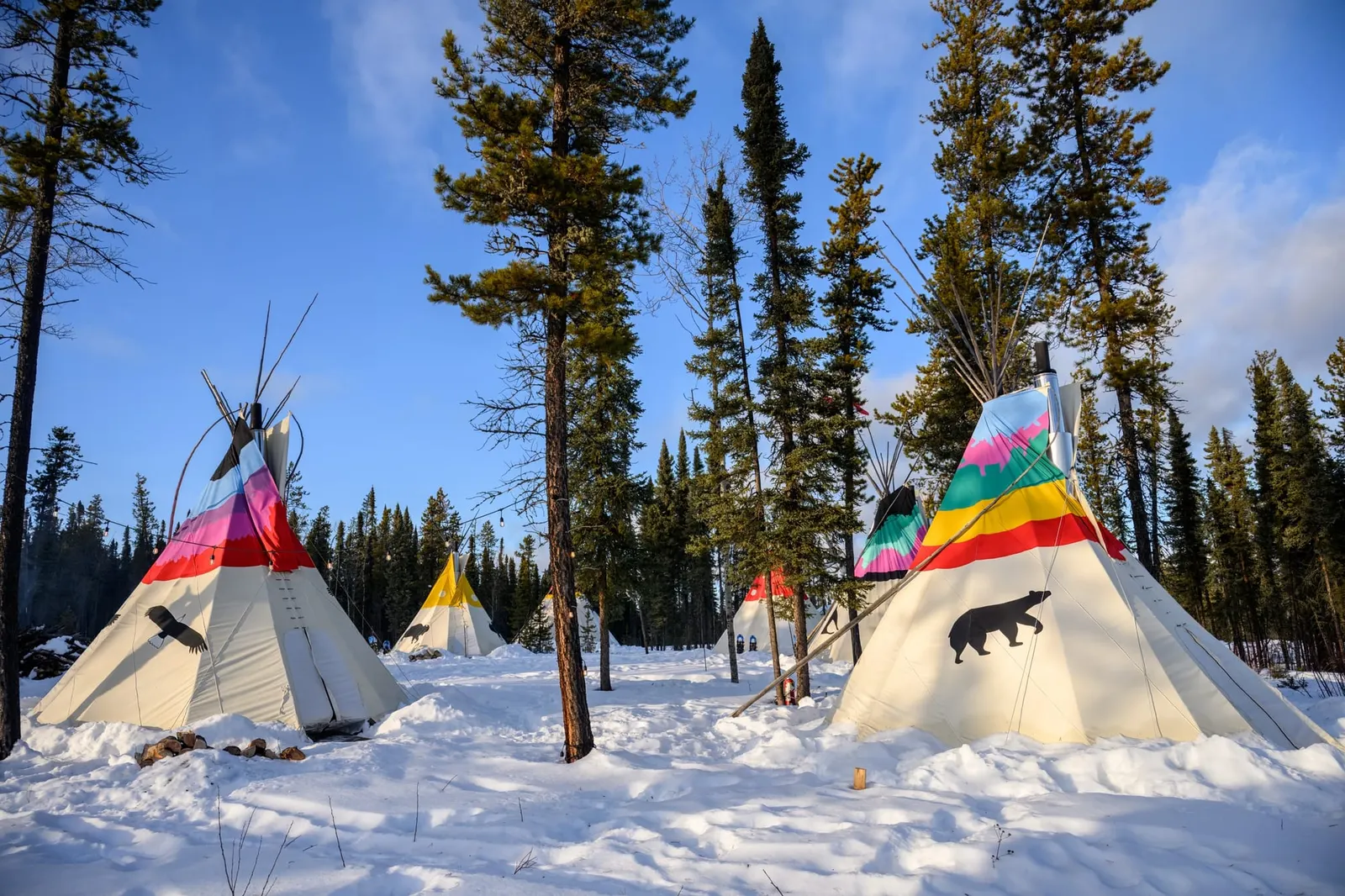 Painted tipis among spruce trees in deep snow at the Aurora Borealis Indigenous Village