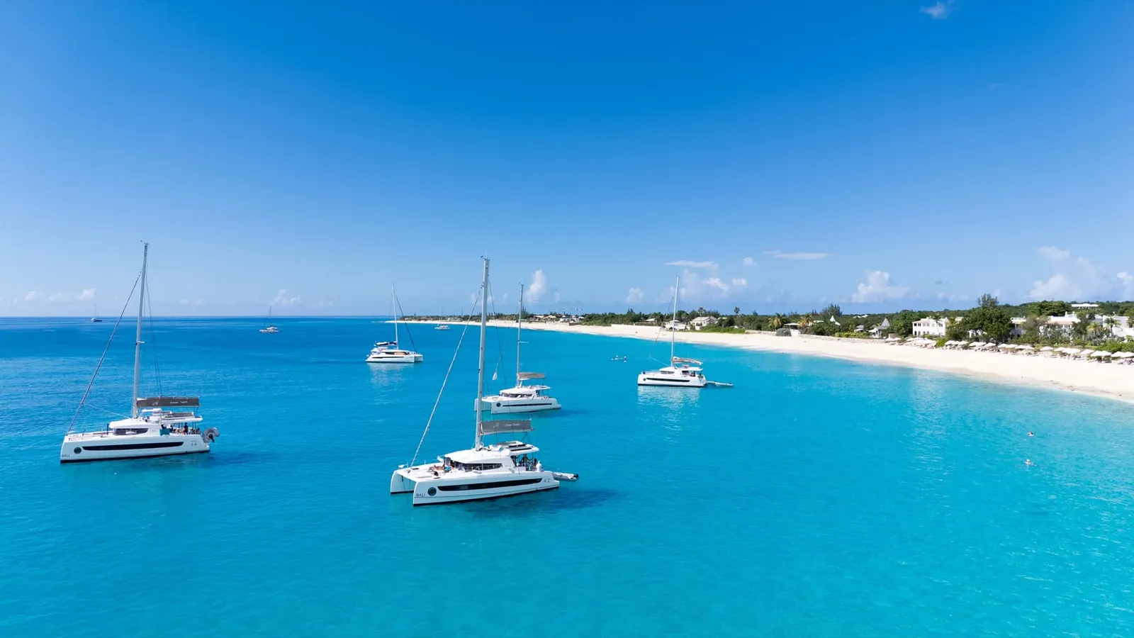 Catamarans anchored in turquoise water off a long white beach lined with umbrellas