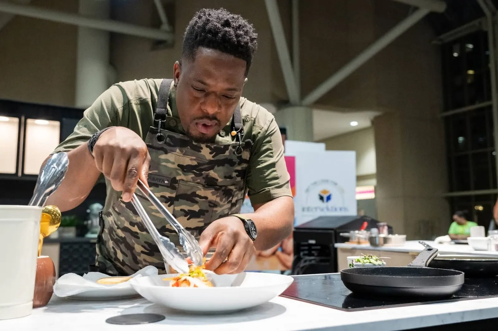 Chef Noel Cunningham plating food with tongs at a festival cooking demonstration