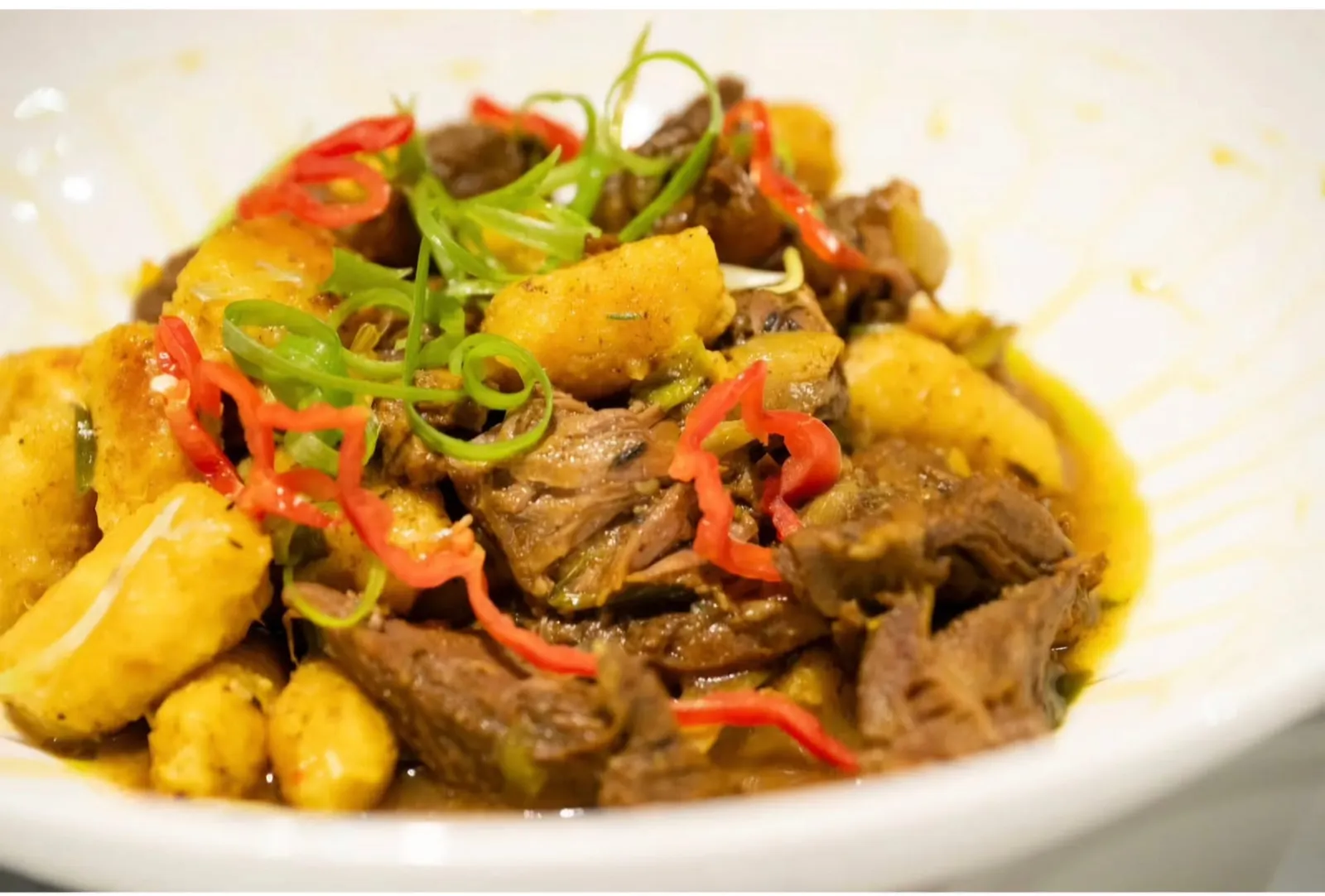 A bowl of braised meat with plantain, sweet peppers and sliced green onion