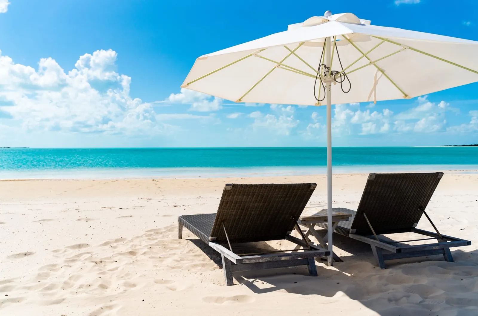 Two loungers under a white umbrella on a white-sand beach facing turquoise water