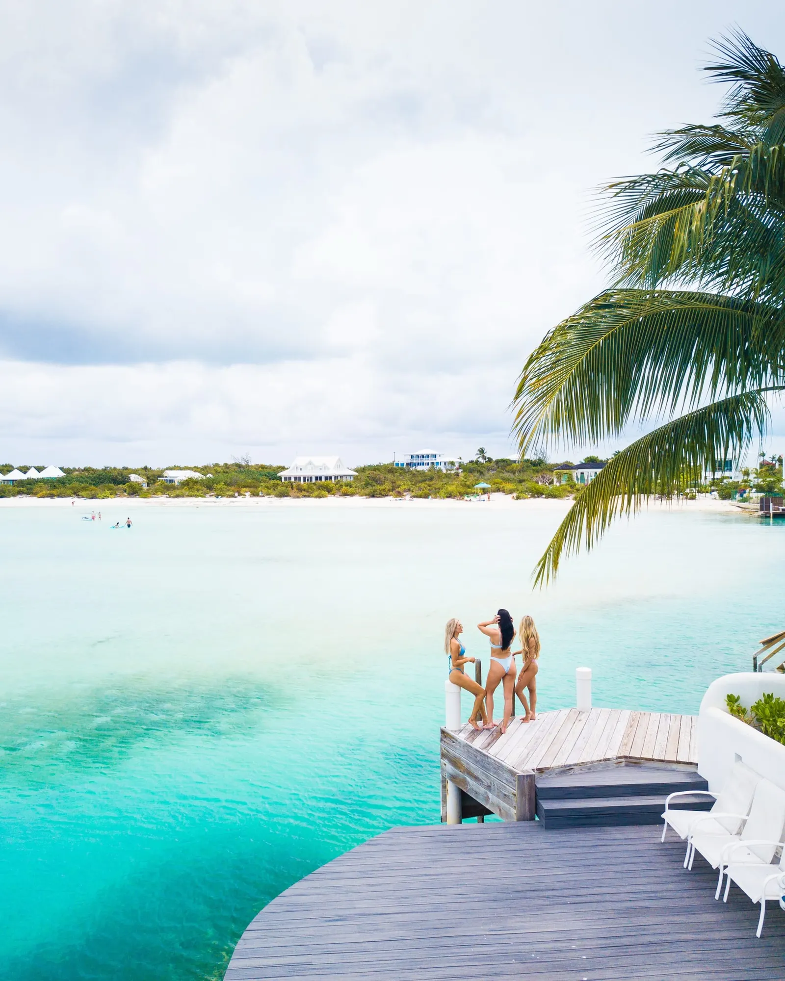 Two women relaxing on a wooden dock above clear turquoise water