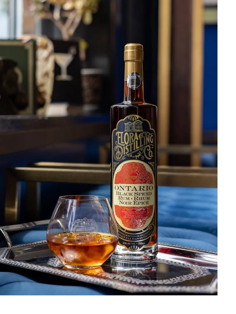 A bottle of Elora Distilling Co. Ontario Black Spiced Rum on a silver tray beside a glass poured over ice