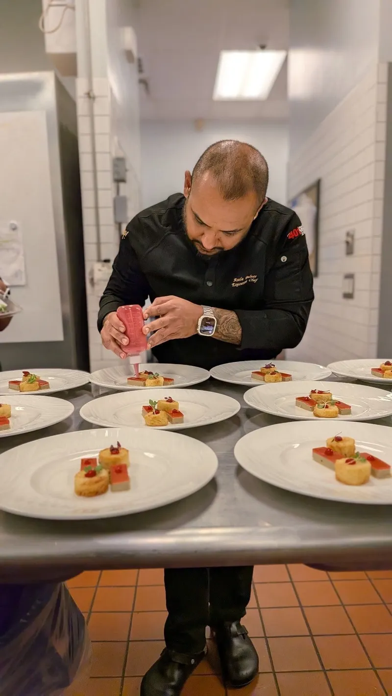 Chef Asela Bulner in black chef whites piping garnish onto a line of plated desserts