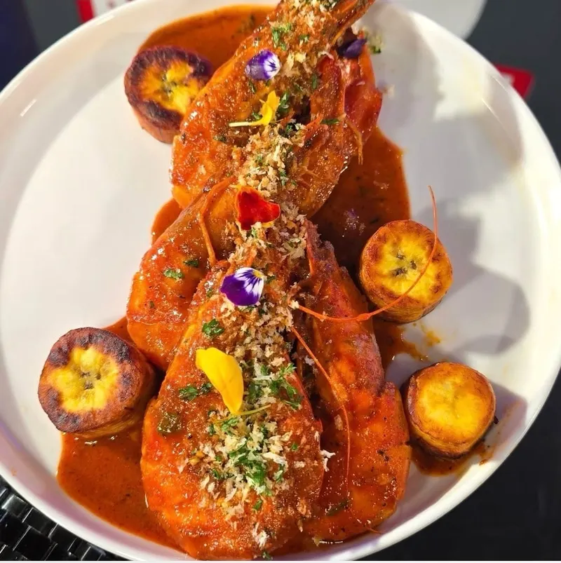 Shrimp in a rich red sauce with fried plantain rounds and edible flowers