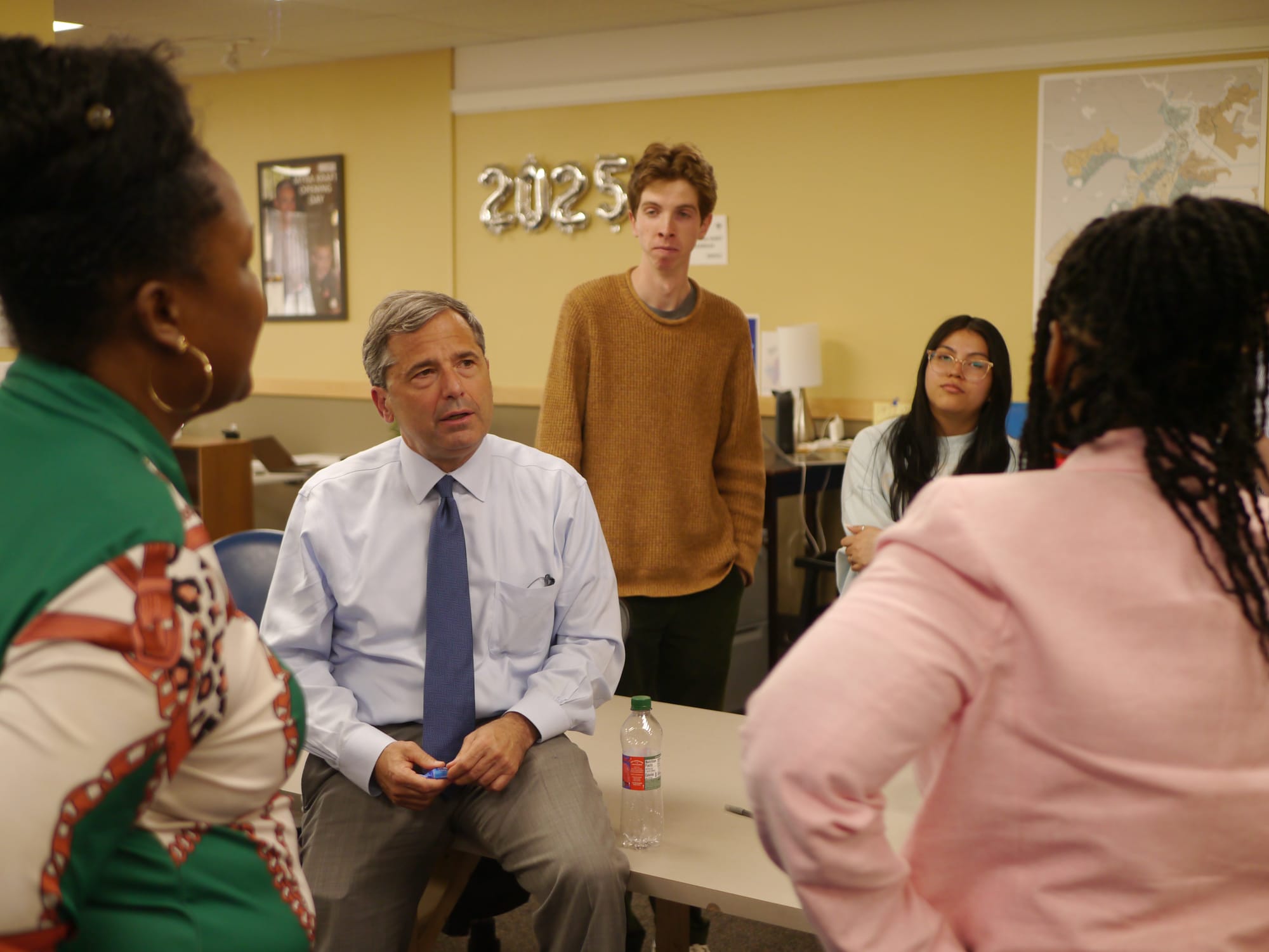 Seated on a desk, Josh Kraft chats with several campaign staff and volunteers at his Nubian Square campaign office. 