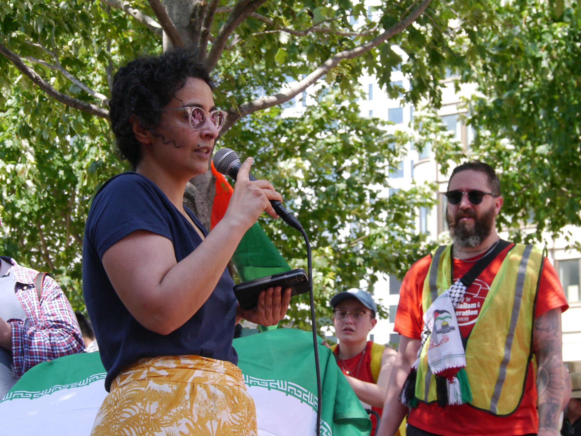 Iranian American scientist Bahar Sharafi, holding a microphone, addresses demonstrators at the JFK Federal Building. 
