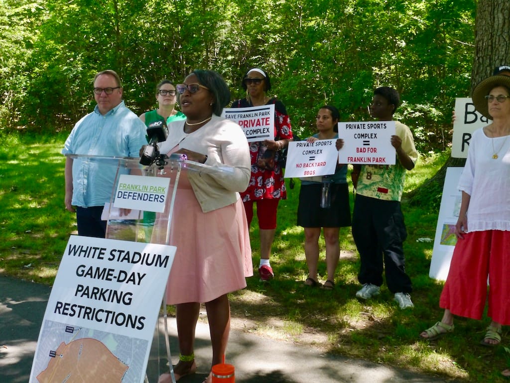 Renee Stacey Welch speaks to reporters. Behind are people with signs opposing privatization of White Stadium.