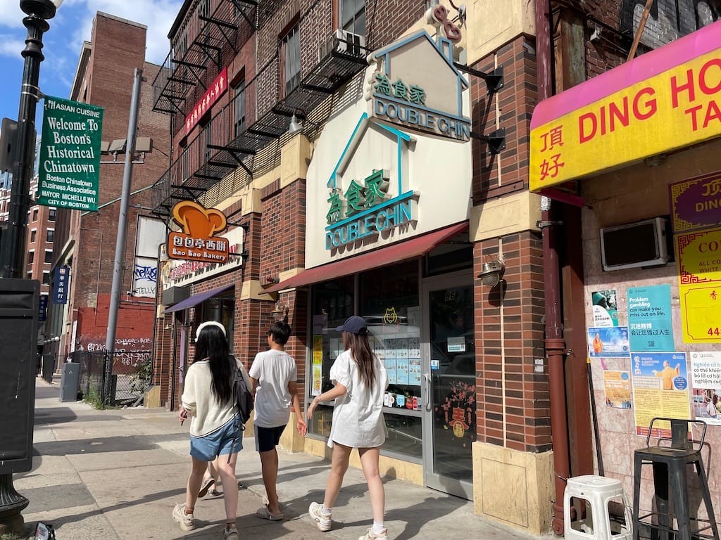 A group of four teenagers walking past the Double Chin restaurant entrance on Harrison Avenue in Chinatown.