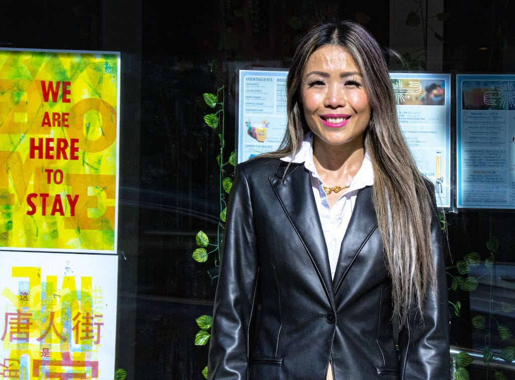 Gloria Chin stands next to a sign reading "We are here to stay."