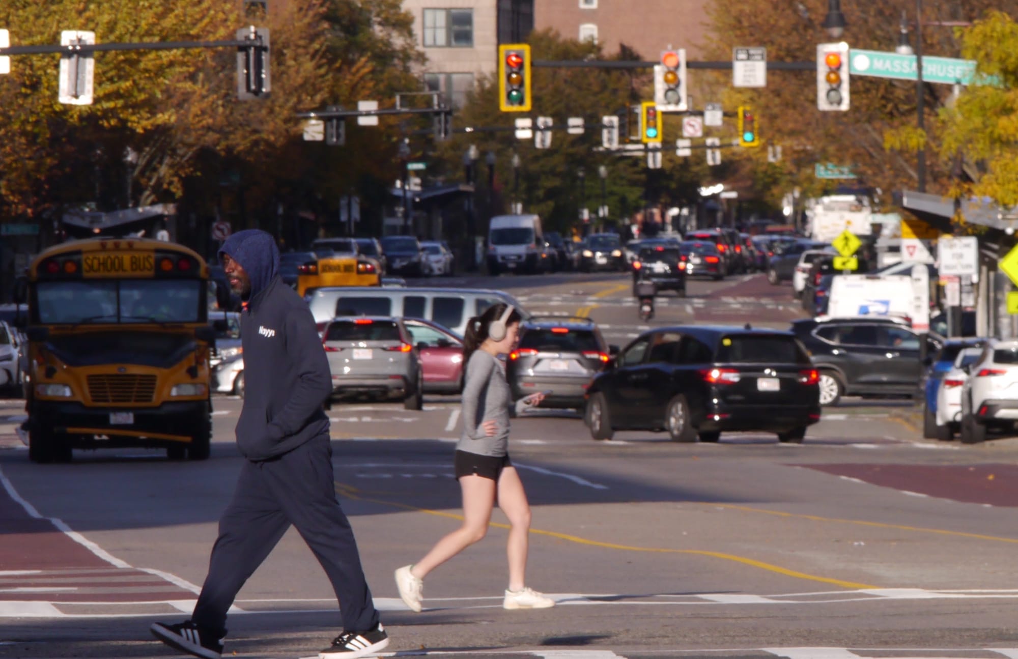 A Black man heads south west in the pedestrian crossing at Washington and Lenox streets while an Asian woman jogs in a northeast direction.