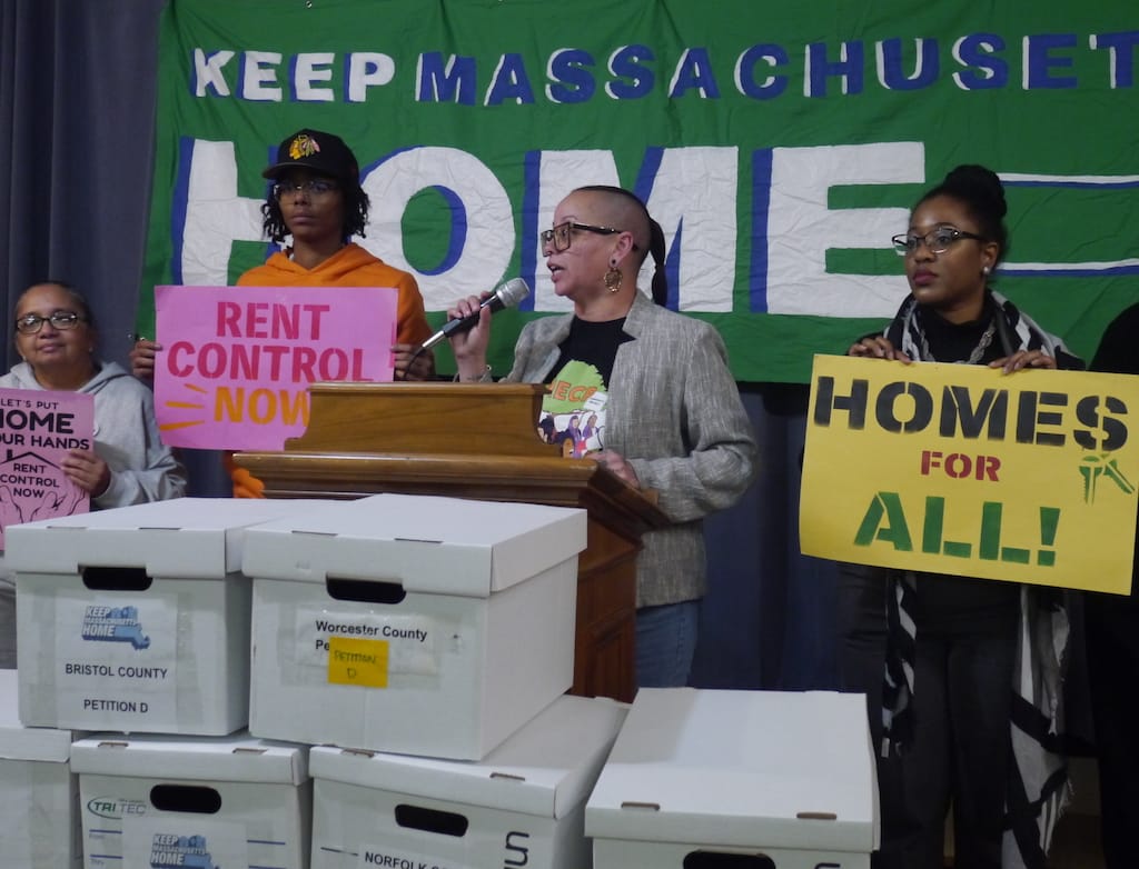 Mimi Ramos speaks to activists in the Church on a Hill in standing before boxes of signatures.