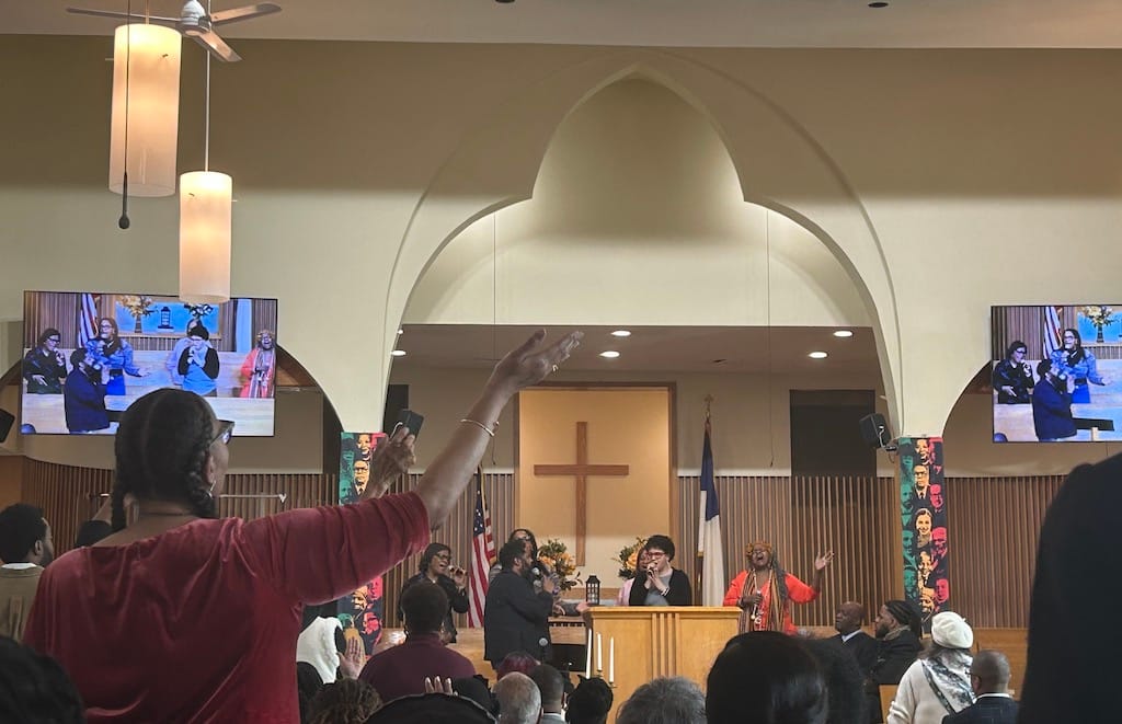 A worshiper in the audience raises her arm while a worshiper at the pulpit leads congregants in song at the 12th Baptist Church in Roxbury.