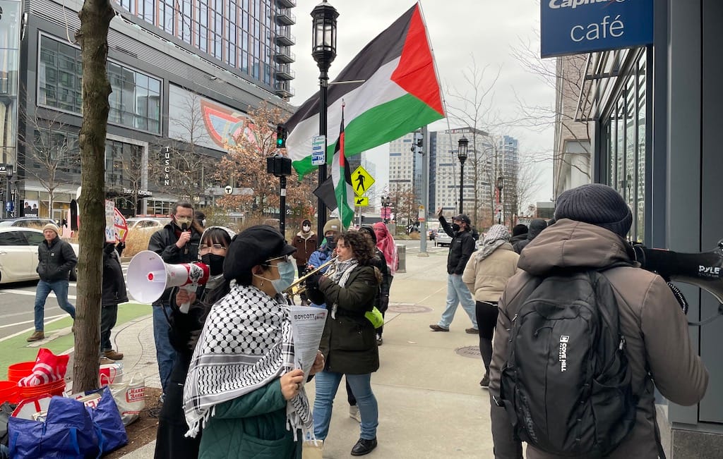 Demonstrators carrying Palestinian flags, leaflets, bullhorns and a trumpet picket in front of the Capital One Cafe on Seaport Boulevard.