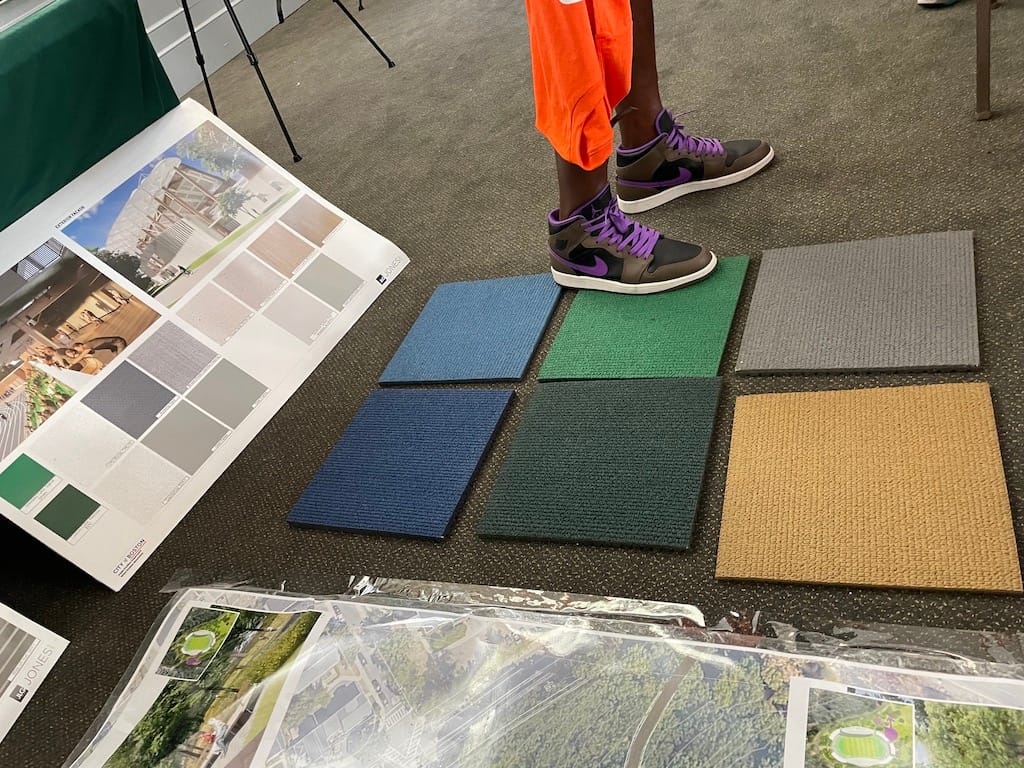 A man stands on carpet swatches laid out in front of a rendering of the interior of a grandstand.