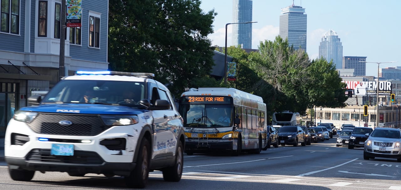 A police cruiser with blue lights flashing races through the intersection of Warren and Moreland streets in Roxbury.