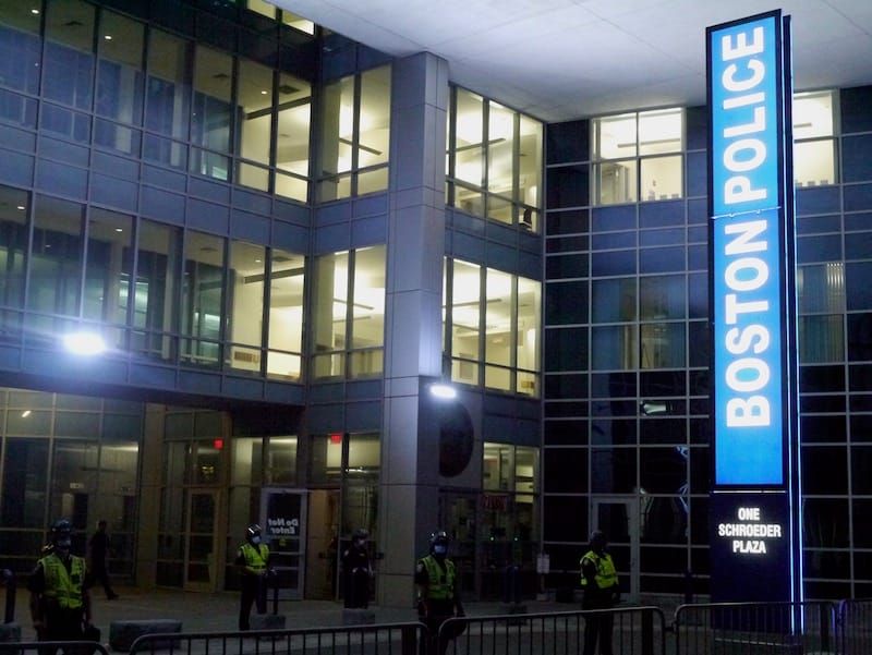 Entrance to Boston Police Department headquarters with officers in riot gear standing in front.