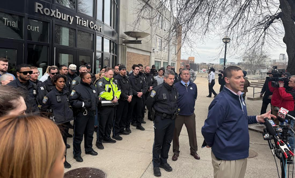 Uniformed Boston Police officers line up in front of Roxbury District Court as Boston Police Patrolmen's Association President Larry Calderone addresses reporters.