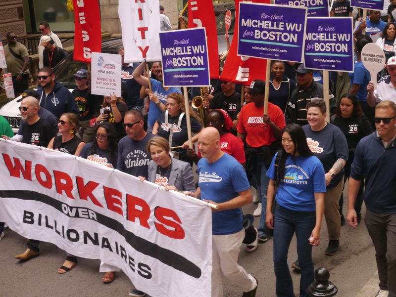 Labor leaders march behind a banner that reads "Wokers over billionaires" while marching through downtown Boston.