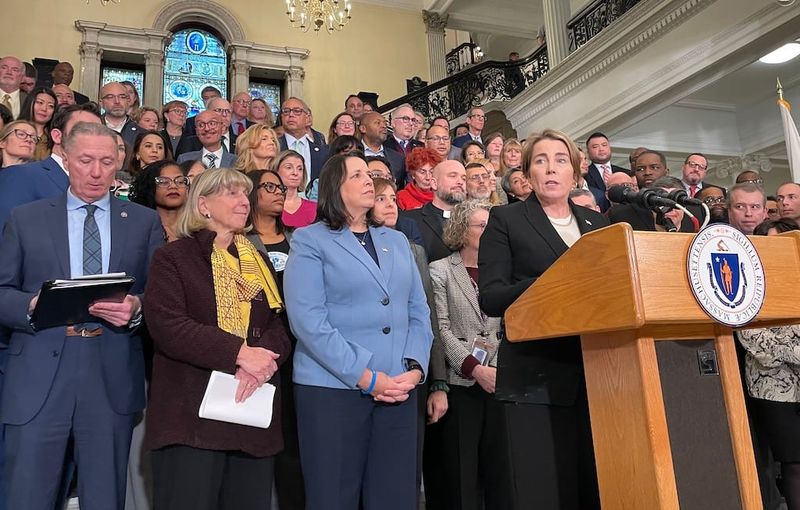 Governor Maura Healey, backed by legislators and community members, addresses reporters at the Grand Staircase in the State House.
