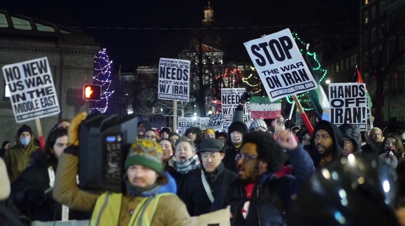 Protestors holding signs with anti-war slogans march near Park Street Station.