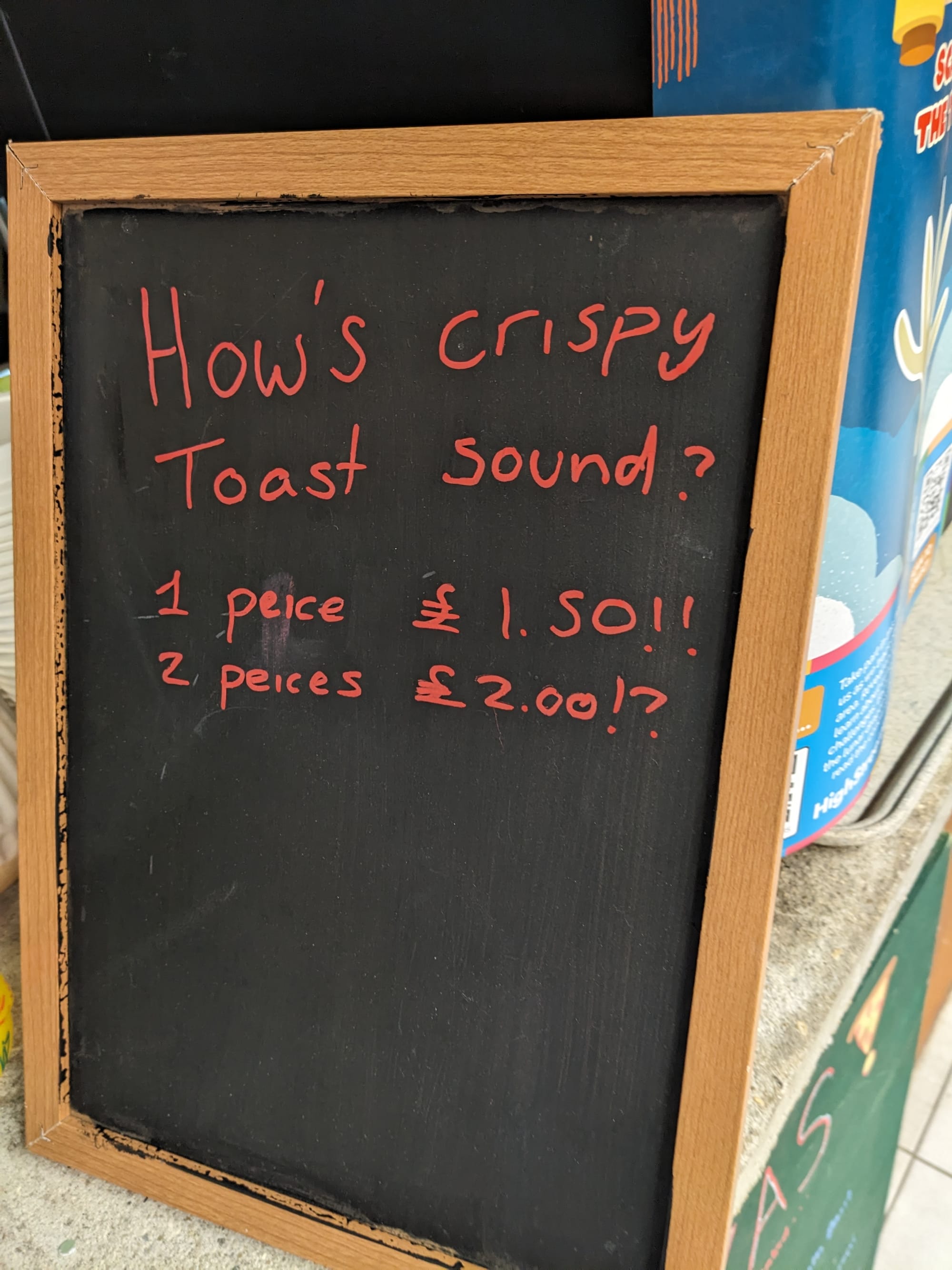 A chalkboard in a cafe with misspellings. It reads: "How's crispy toast sound? 1 peice £1.50! 2 peices £2.00!?"