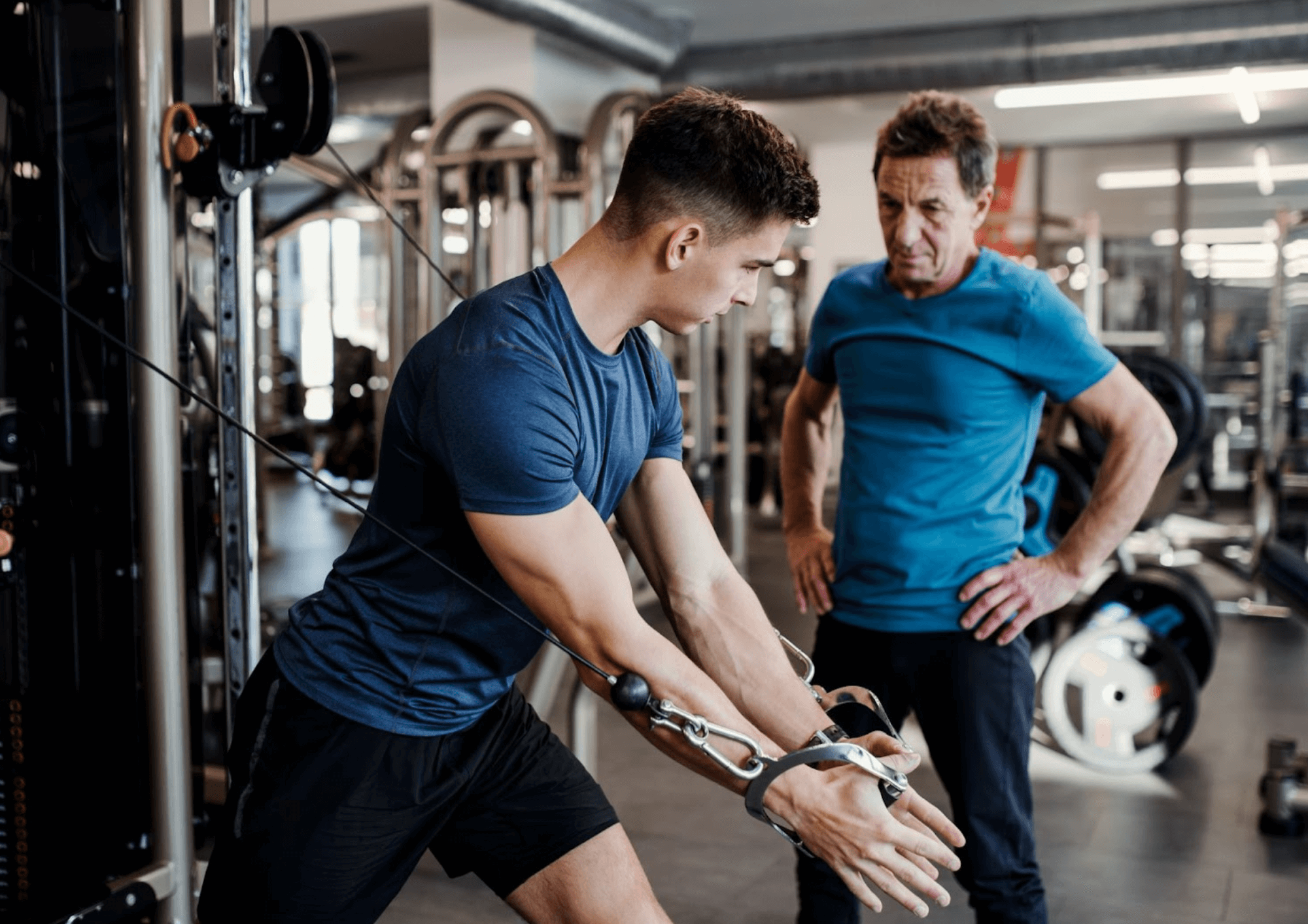 Young man is performing an exercise in a gym. Physiotherapist is watching over him.
