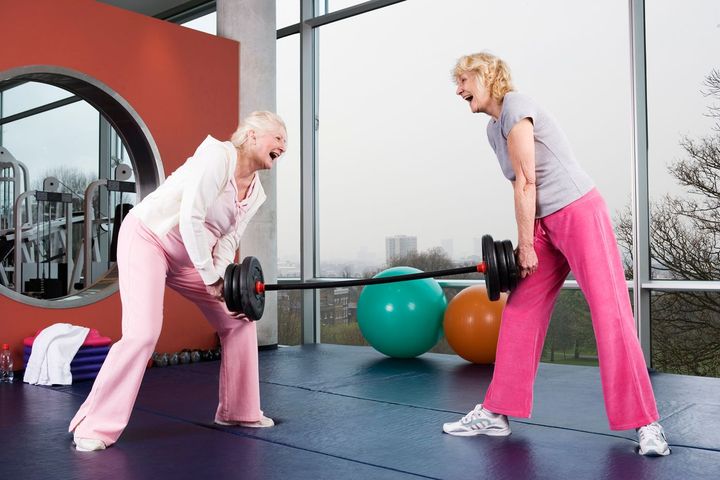 Two older women lifting either end of a mini barbell. 