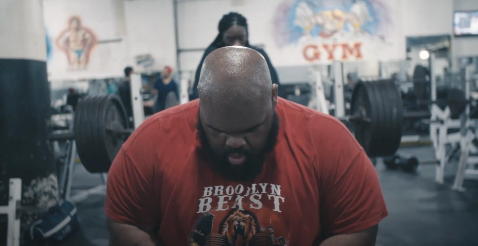 a man wearing headphones sitting in a gym with his head bent wearing a "Brooklyn Beast' t shirt