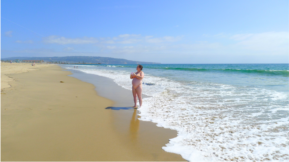 a 7 months pregnant woman flying a kite at a beach