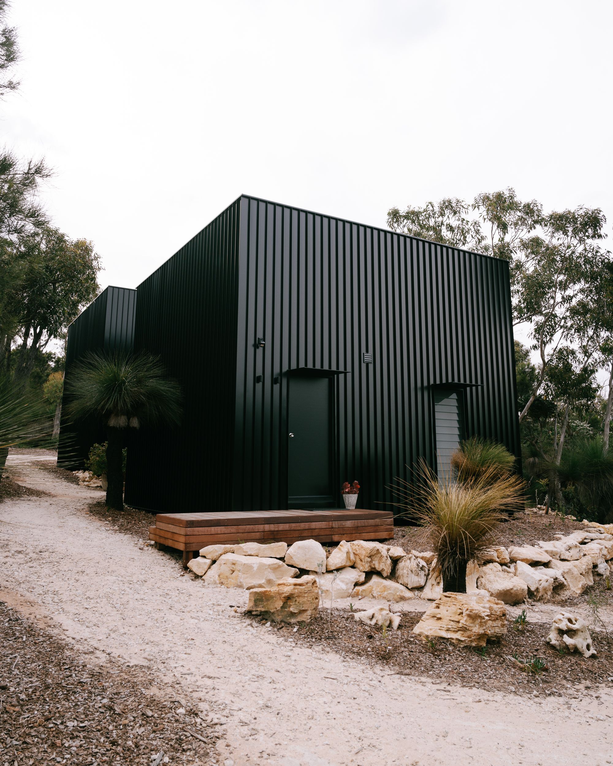 An external view of DEN PLACE showing the two accommodations with black metal cladding sitting in the landscape