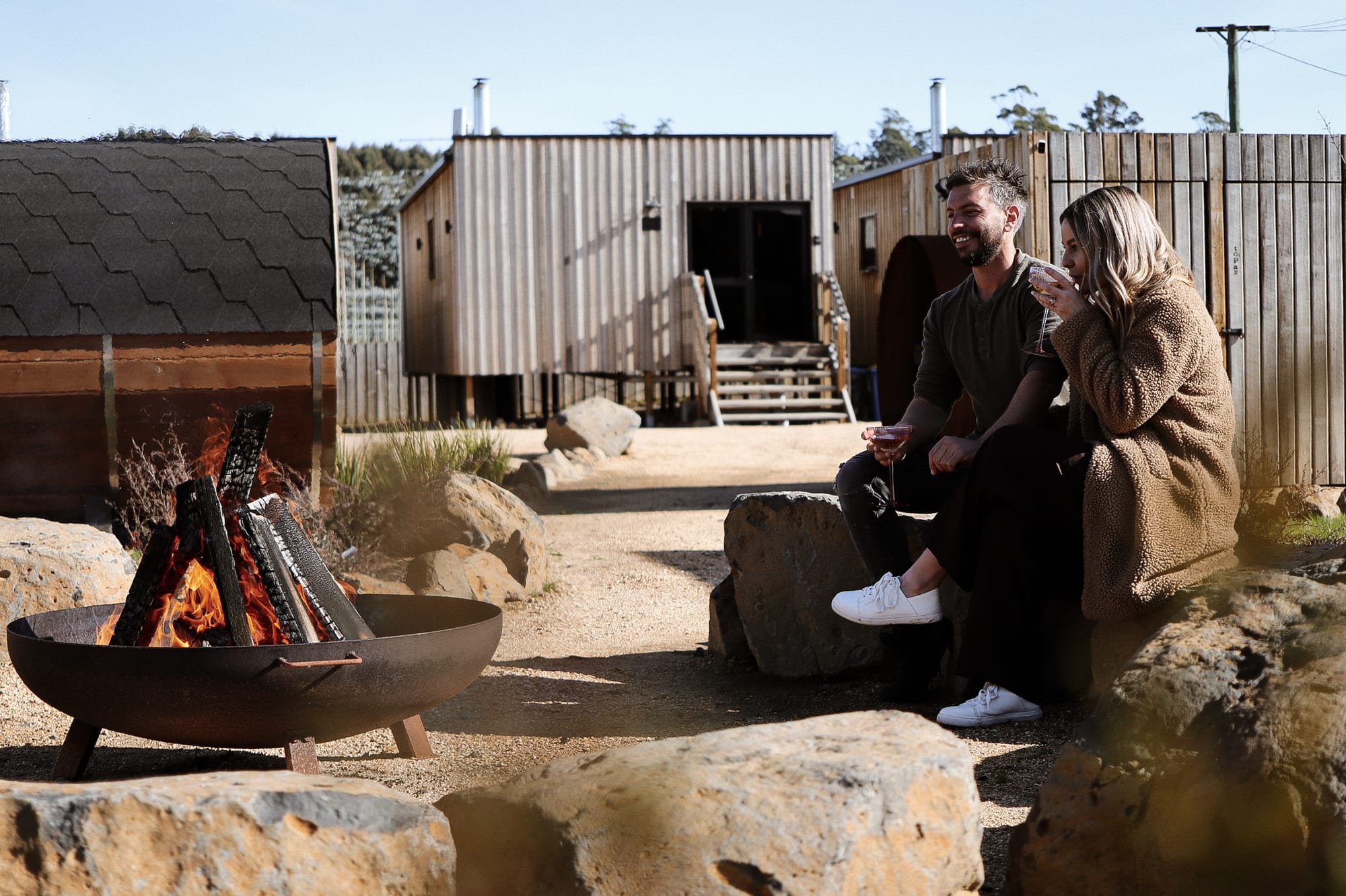 Just Down the Road. Photographer: Studio Winslow.A wooden wall of a modern structure with vertical planks, featuring two small, closed doors and showing the clear blue sky above.