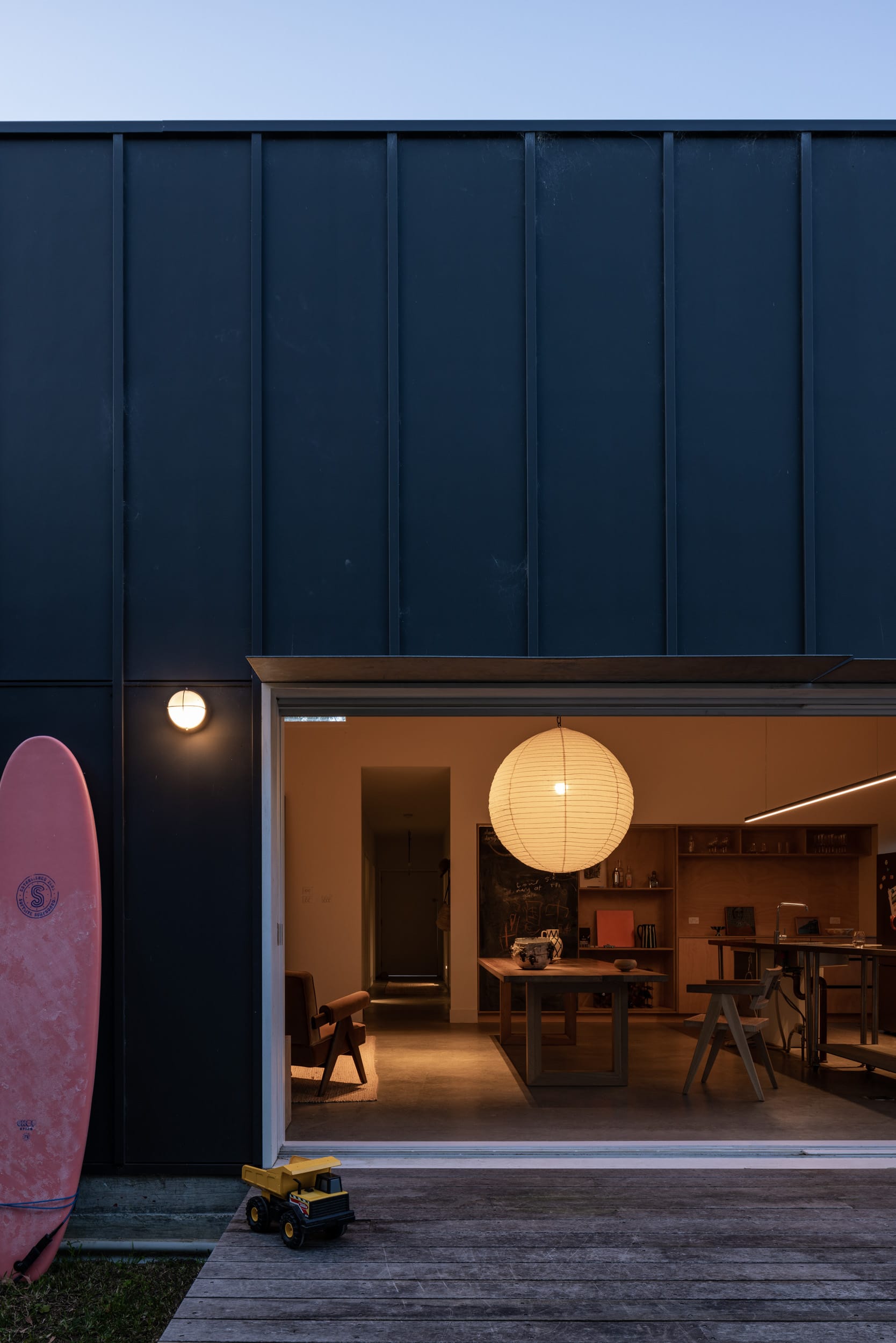 Drip-Dry House by Marker Architecture & Design. A read shot of the beach house open up at dusk showing the timber deck and the large pendant light over the timber dining table