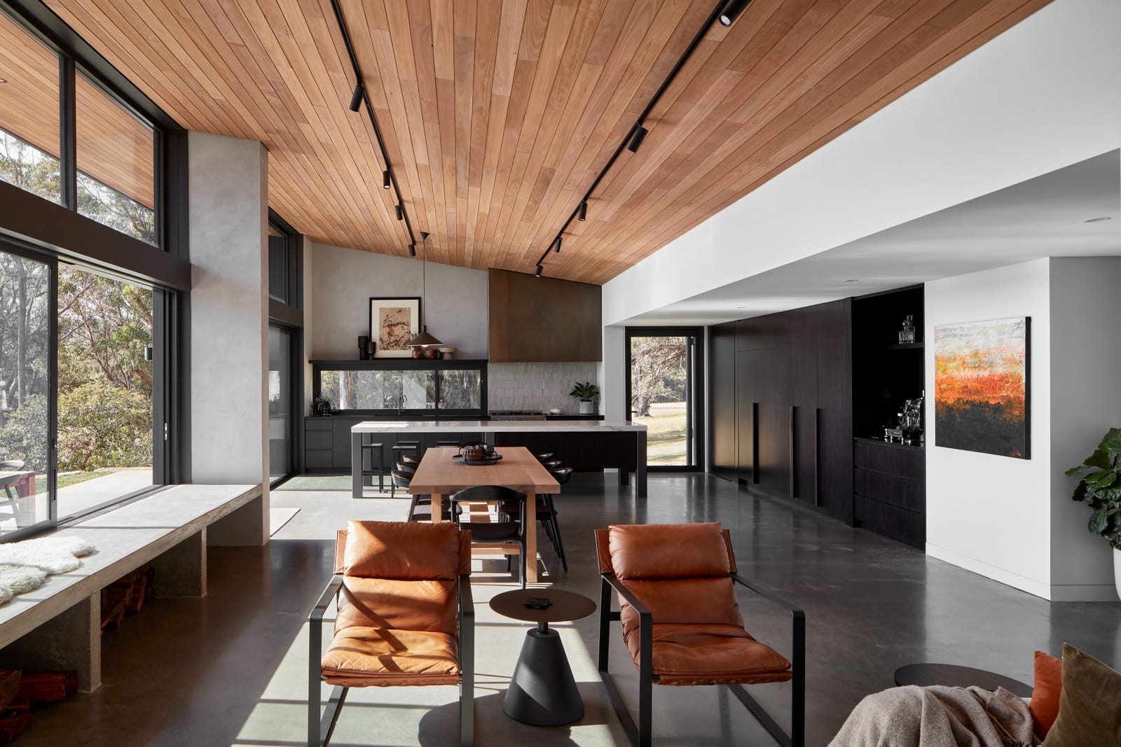 House Woodland by AO Design Studio. An exterior view of House Woodland by AD Design Studio, highlighting the modern architectural design with a mix of materials. The facade combines wood siding with black metal panels. The house has large windows and sliding doors, integrating indoor and outdoor spaces. A wooden deck extends from the house, furnished with an outdoor dining area.