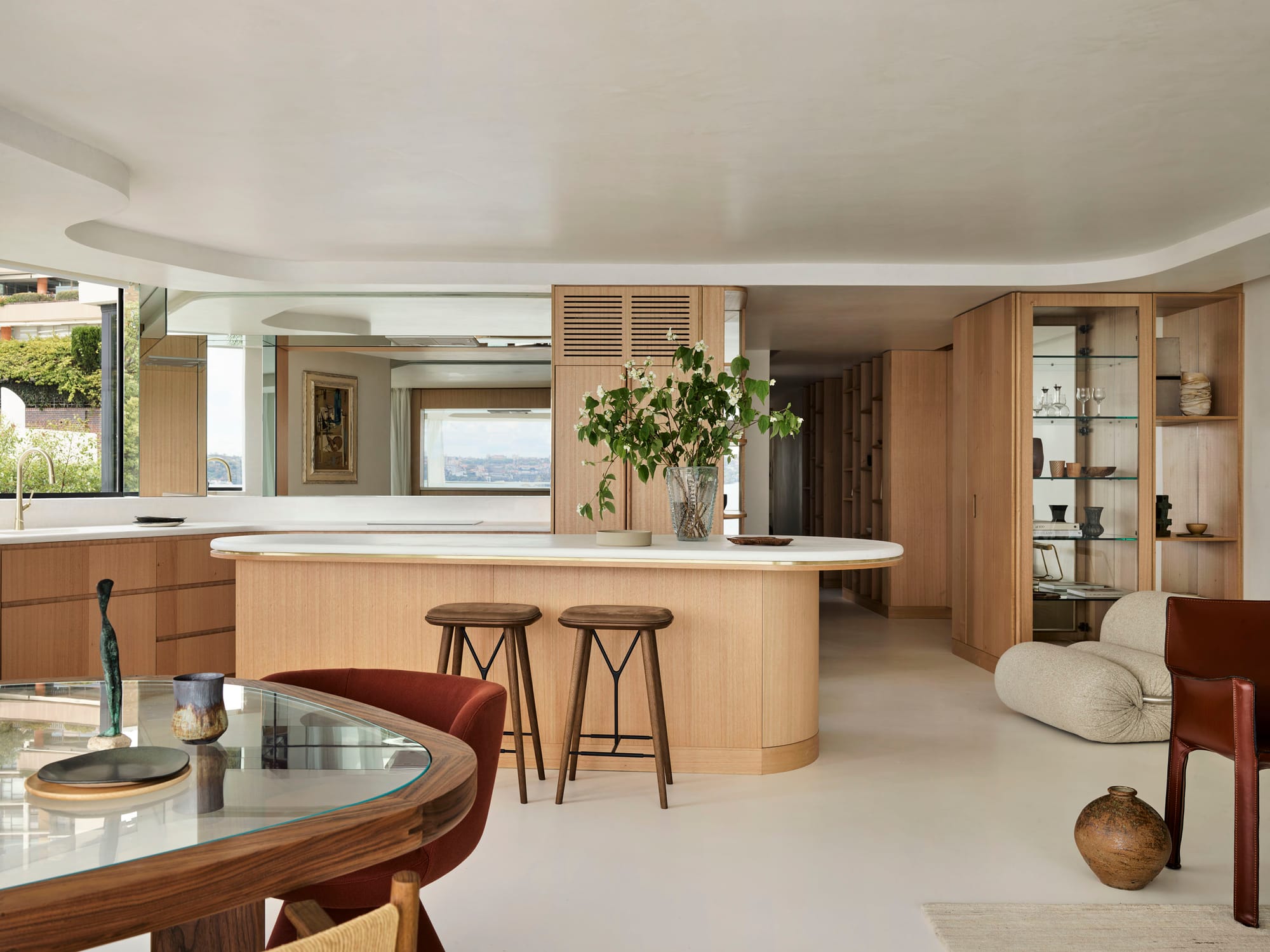 Tasmanian Timber Series: Darling Point Apartment. Photography by Ansen Smart. Wide angle image of kitchen and living space in residential apartment. Tasmanian Oak organically curved kitchen island, kitchen benches and cabinetry in far right of image. Polished white floors and recessed white organically curved ceiling. 