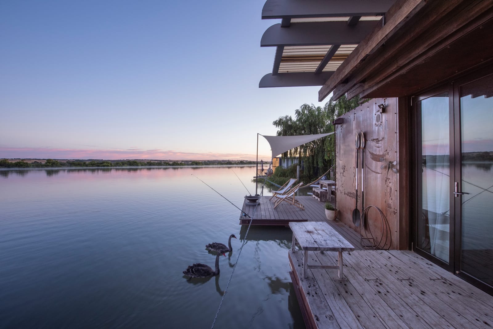 Bill's Boathouse. An exterior shot of the boathouse at dusk showing two swans swimming up to the boathouse