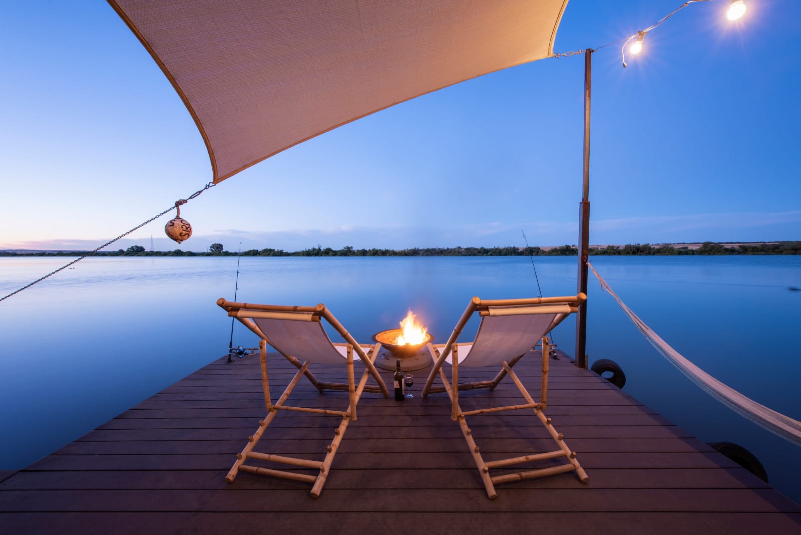 Bill's Boathouse. An exterior shot from the timber deck showing two lounge chairs and an outdoor fire pit looking over the river