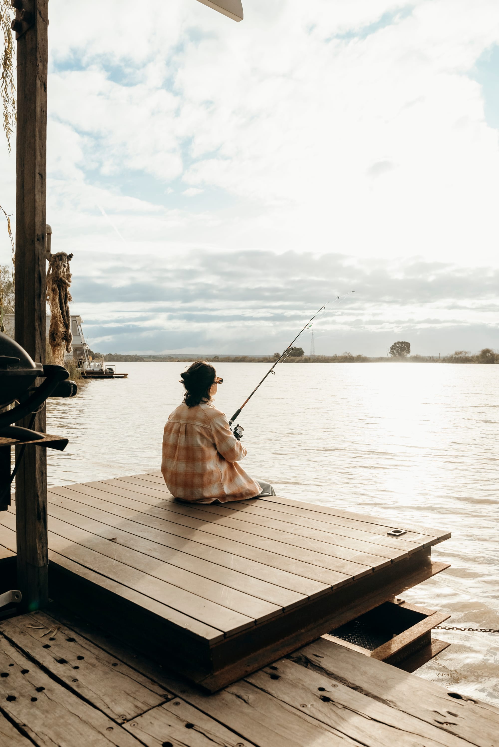 Bill's Boathouse. A woman fishing from the timber deck of the boathouse