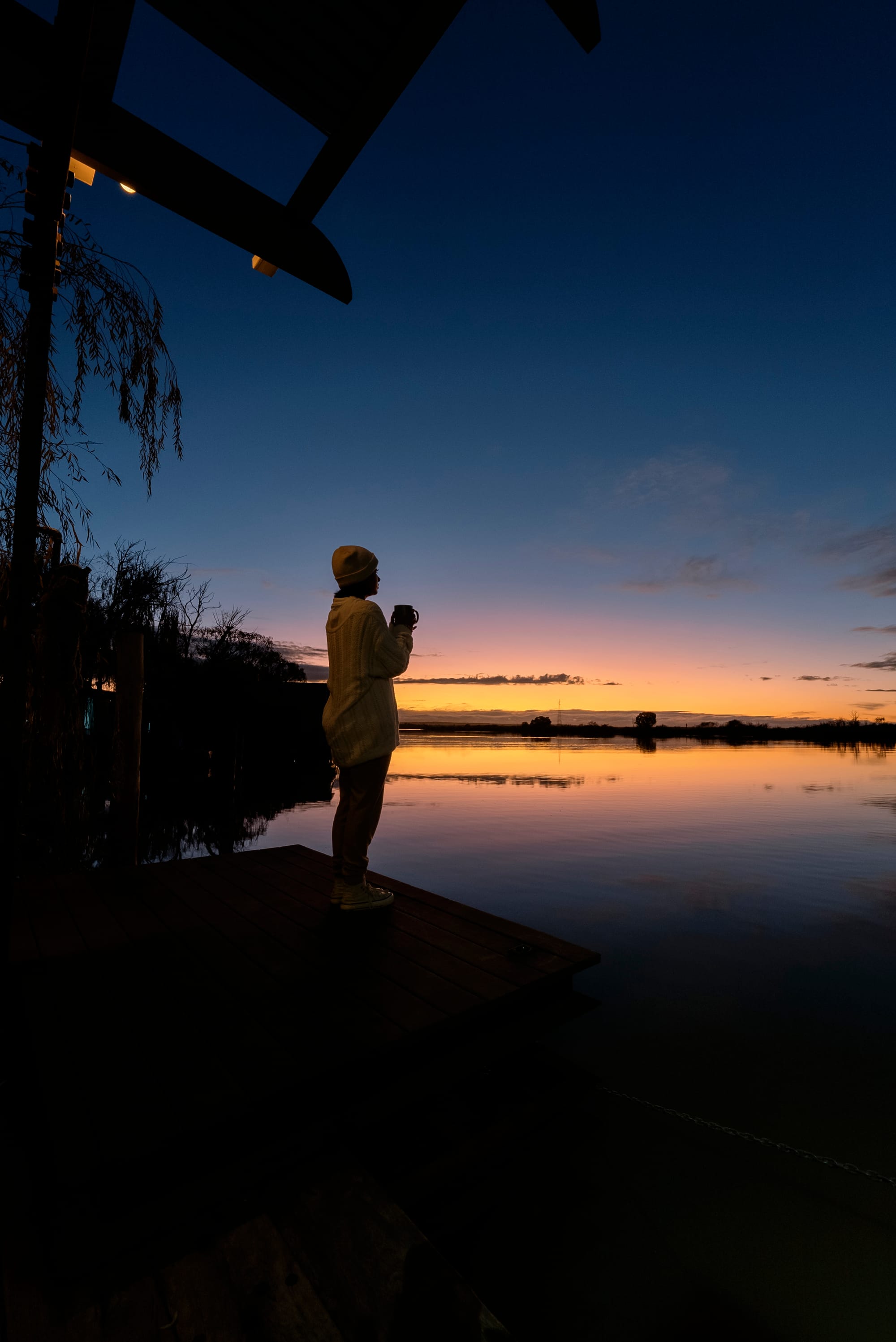 Bill's Boathouse. A sunset shot showing a woman drinking a cup of coffee and looking out over the river