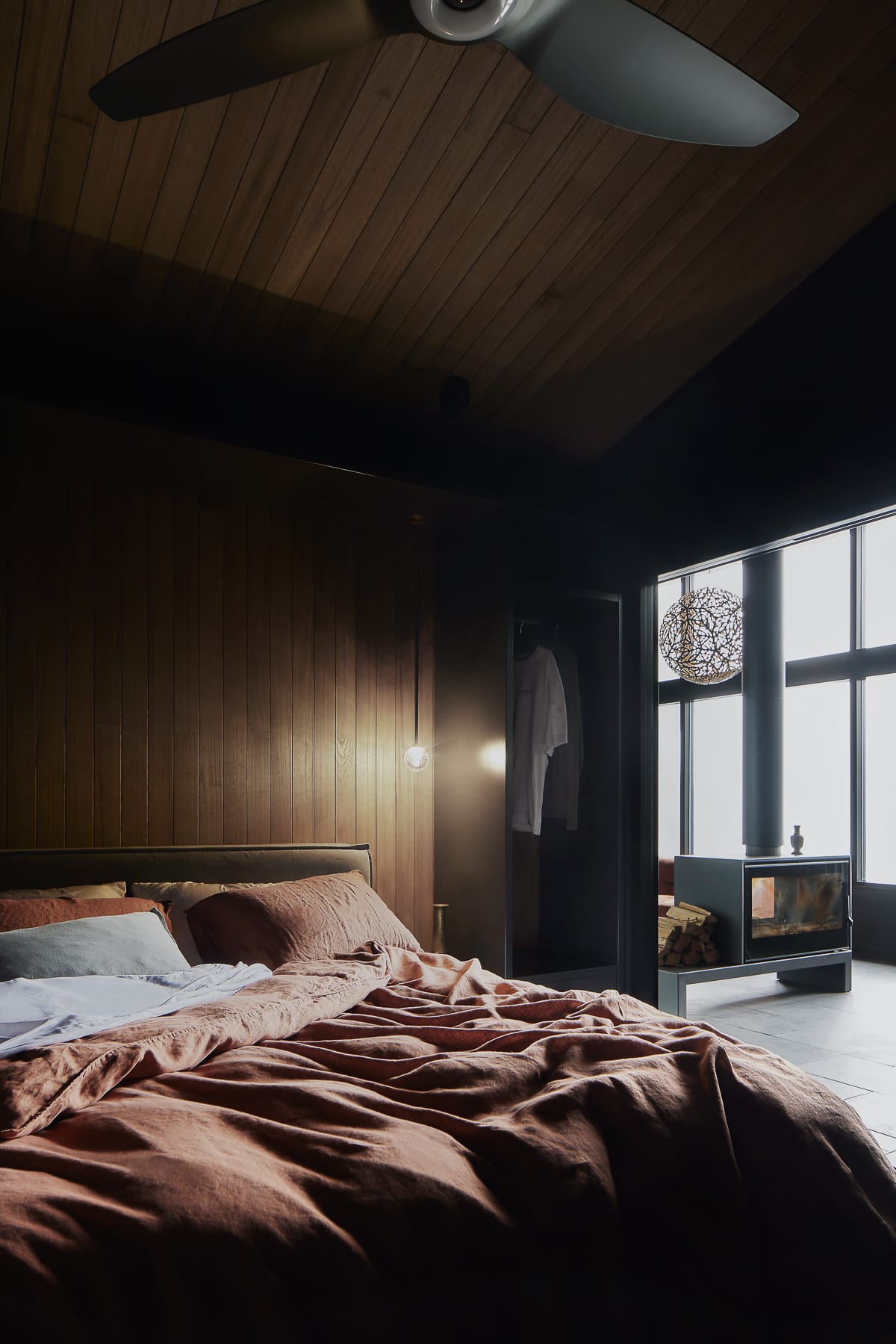 An interior shot of the bedroom in the cabin showing a warm space right next to the fireplace with red linen covers