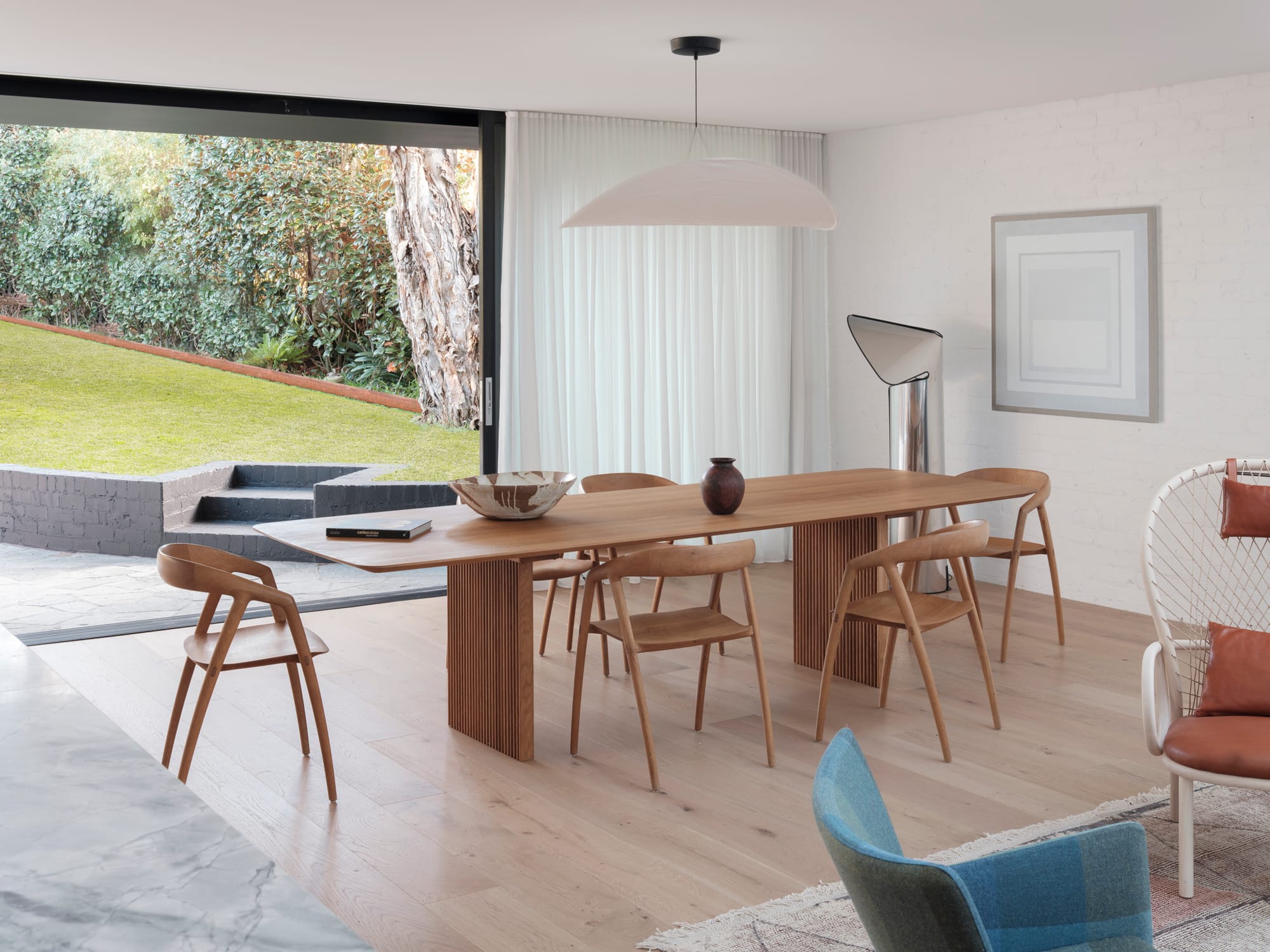Bellevue House by Carla Middleton Architects. Photography by Tom Ferguson. Long timber dining table. Floor-to-ceiling sliding door runs length of back wall, opening onto green backyard. 